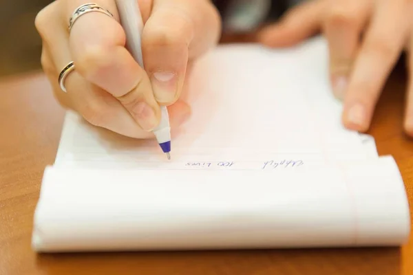 Een close-up van de hand van een vrouw die een pen vasthoudt en iets schrijft in een handboek. — Stockfoto