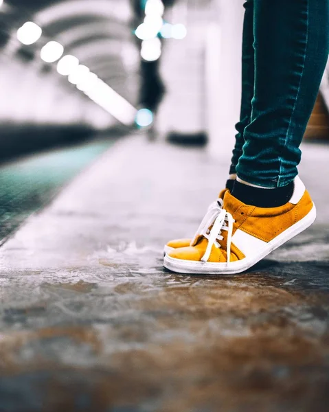 Sarı ve beyaz spor ayakkabılar ve mavi dar pantolon giyen birinin dikey yakın plan çekimi. — Stok fotoğraf
