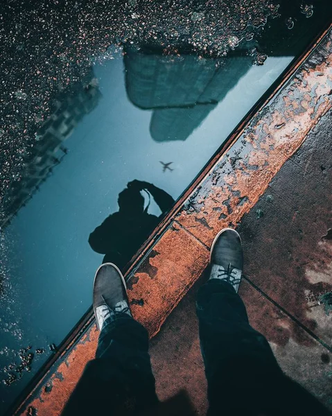 Verticale opname van de reflectie van een persoon en gebouwen in een waterplas — Stockfoto