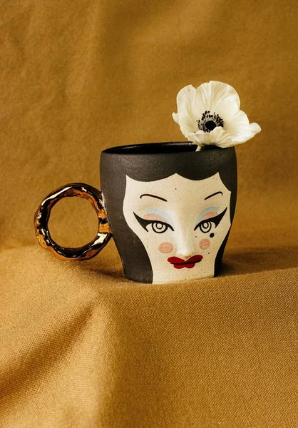 Plan vertical de tasse noire avec visage féminin avec une fleur blanche sur fond brun — Photo