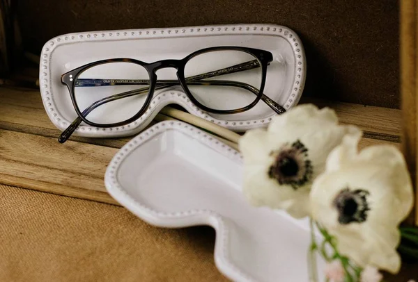 Gafas graduadas y estuches en blanco y negro decorados con flores blancas sobre una superficie de madera —  Fotos de Stock
