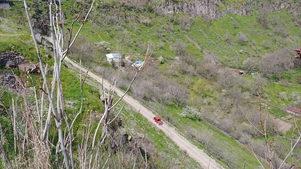 Alto ángulo de tiro de una estrecha carretera de grava con un coche rojo en las verdes colinas de Armenia —  Fotos de Stock