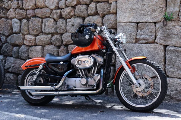 Червоний мотоцикл з шоломом, що висить на кермі з кам'яною стіною на задньому плані. — стокове фото