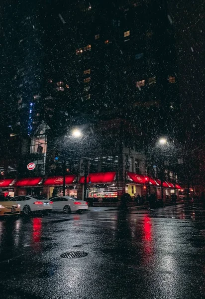 Straat vol auto 's, straatverlichting en een hoog gebouw op een regenachtige avond — Stockfoto