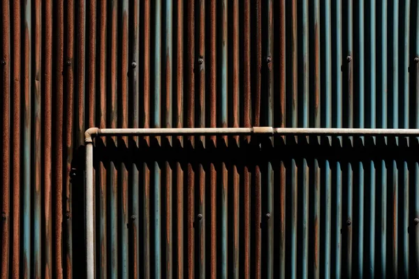 A brown metal tube on the background of brown and blue rusty poles