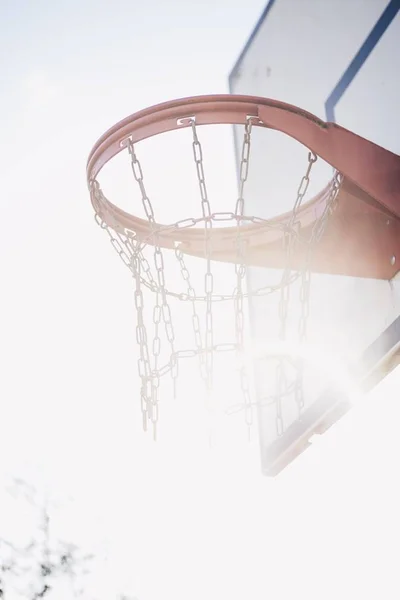 Tiro vertical de ângulo baixo de um aro de basquete com um céu brilhante no fundo — Fotografia de Stock