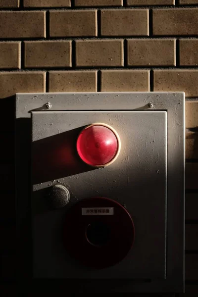 Vertical closeup shot of a security red alarm light on a gray box on a brick wall