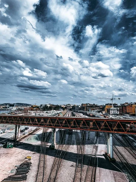 Σιδηρόδρομοι και πολύχρωμα κτίρια κάτω από μια μακρά γέφυρα με το φόντο των όμορφων νεφών — Φωτογραφία Αρχείου