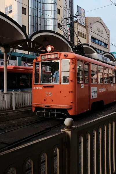 Binaların yakınındaki bir tren istasyonunda rayüzerinde kırmızı bir trenin dikey çekimi — Stok fotoğraf