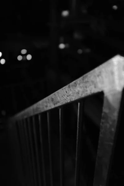 Grayscale vertical tiro close-up seletivo de um corrimão de aço em um fundo preto embaçado — Fotografia de Stock