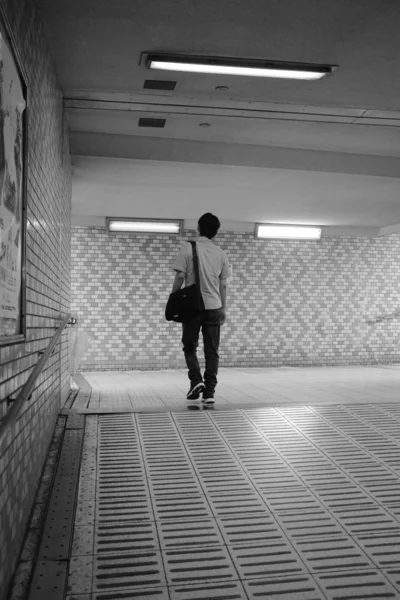 Skala odcieni szarości pionowy strzał męskiego chodzenia w miejscu z ceglanymi ścianami z poręczami stalowymi — Zdjęcie stockowe
