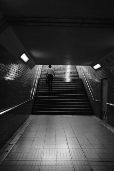 Vertikální záběr osoby šplhání do podzemních schodů s ocelovými zábradlím na cihlových stěnách — Stock fotografie