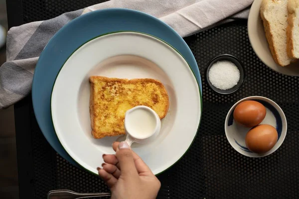 Vue aérienne d'une personne versant de la crème sur un pain perdu près des œufs et du sucre — Photo