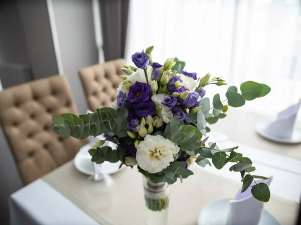 Selektiv närbild skott av lila och vita blommor och gröna blad inuti en glasvas på ett bord — Stockfoto