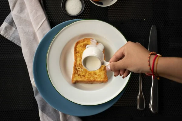 Vue aérienne d'une personne versant de la crème sur un pain grillé français sur une assiette ronde blanche — Photo