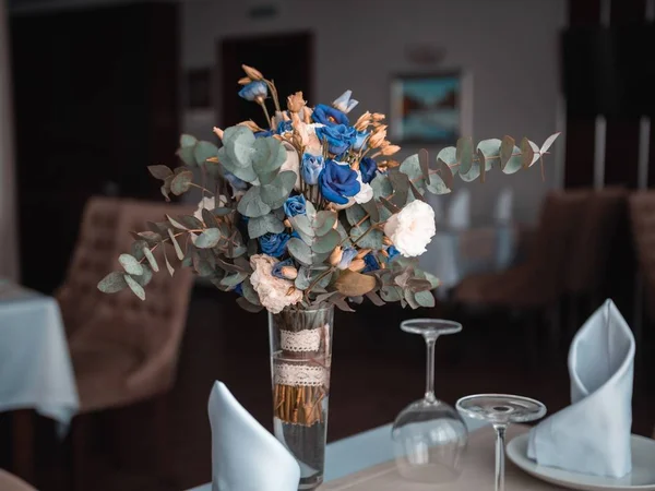 Επιλεκτική κοντινή φωτογραφία με μπλε και λευκά λουλούδια με πράσινα και πορτοκαλί φύλλα σε γυάλινο βάζο — Φωτογραφία Αρχείου