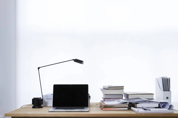 Work desk with a lamp, a laptop, books, and papers on it with a white background — Stock Photo, Image