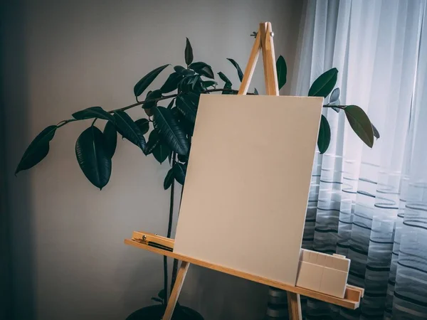 White painting board on a wooden easel near a green plant