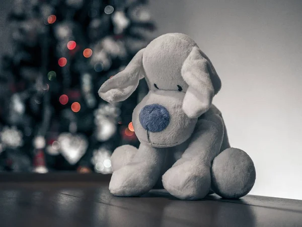 Primer plano de un perro de peluche gris sobre una superficie marrón en el fondo de un árbol de Navidad —  Fotos de Stock