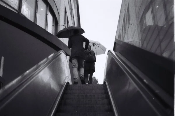 Perspectiva de personas con paraguas bajando de una escalera mecánica desde la estación — Foto de Stock