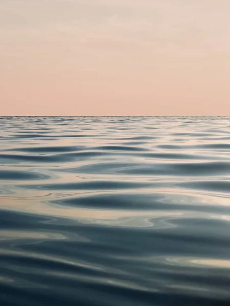 Beau plan vertical de vagues relaxantes d'eau de mer calme sous un ciel rose clair — Photo