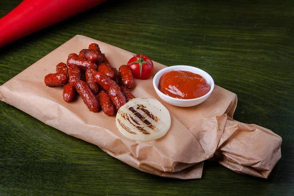Closeup shot of grilled sausages with ketchup, tomato and fried onion on a chopping board — Stock Photo, Image