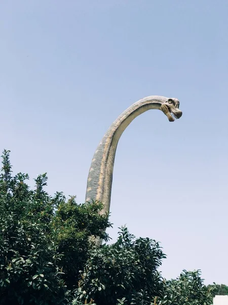 Вертикальный снимок декоративной статуи высокого динозавра-брахиозавра с деревьями внизу — стоковое фото