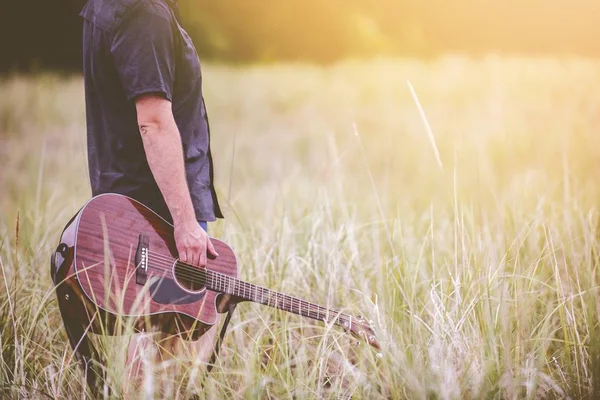 一个人拿着棕色原声吉他站在草地中间的选择性拍摄 — 图库照片
