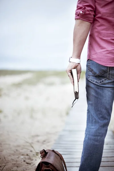 茶色のバッグの近くに立つ厚いノートブックを持つピンクのシャツとジーンズを着た人の垂直選択的なクローズアップショット — ストック写真