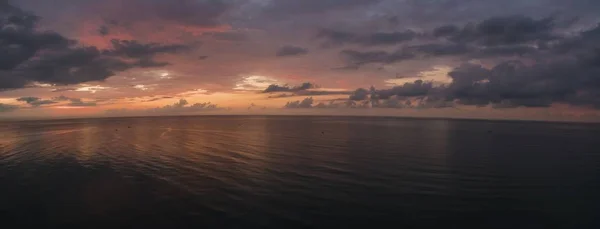 A horizontal shot of a sea under a cloudy sky during sunset