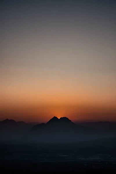 A vertical silhouette shot of mountains under a clear sky during sunset
