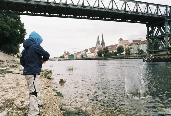 A shot of a person throwing stones in the water surrounded by buildings under the bridge at daytime