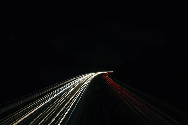 A horizontal timelapse shot of a road with white and red lights at night