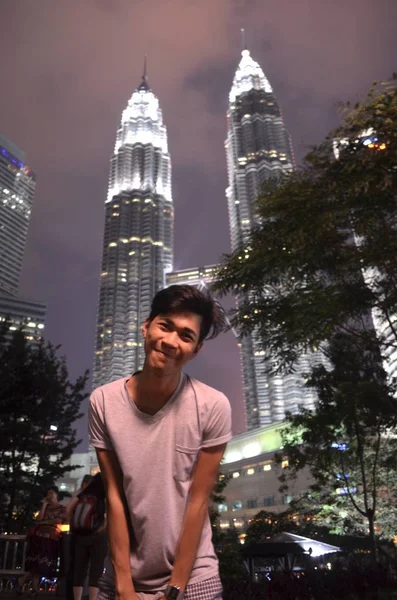 Мужчина, стоящий на фоне башен-близнецов Petronas в Куала-Лумпуре, Малайзия, ночью — стоковое фото