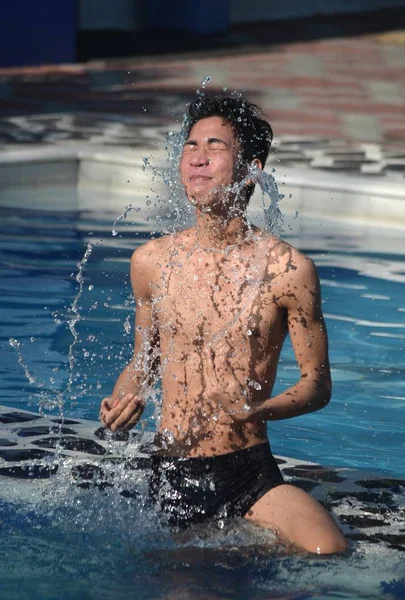 Colpo verticale di un maschio che indossa un costume da bagno nero spruzzandogli acqua in una piscina — Foto Stock