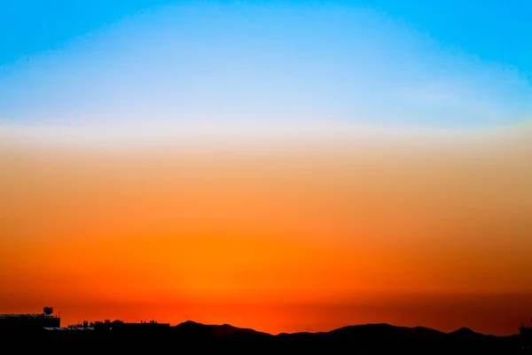 Brede opname van de blauwe oranje lucht bij zonsondergang met gebouwen en bergen zichtbaar op de bodem — Stockfoto