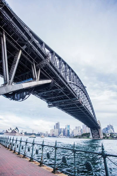 Low angle vertical shot of a bridge over the water with city buildings in the distance — Stock Photo, Image