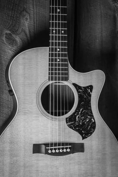 Belle prise de vue en niveaux de gris d'une guitare acoustique appuyée sur une porte en bois sur une surface en bois — Photo