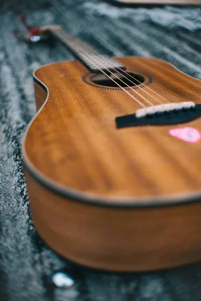 Выборочный фокус на коричневой акустической гитаре на черной поверхности днем — стоковое фото