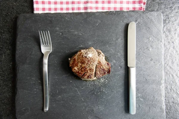 Foto de alto ángulo de un pedazo de bistec sabroso con un tenedor y un cuchillo —  Fotos de Stock
