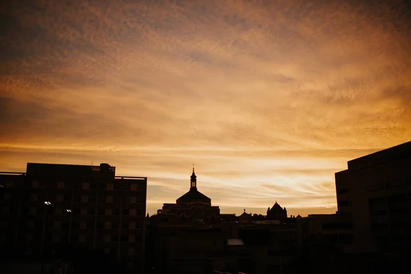 Горизонтальный снимок города на закате с видимым золотым небом и зданиями в силуэте — стоковое фото
