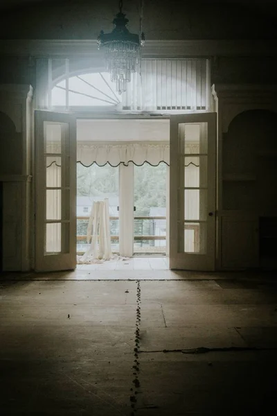 Vertical shot of an empty room with a chandelier on the ceiling and open balcony doors — Stock Photo, Image