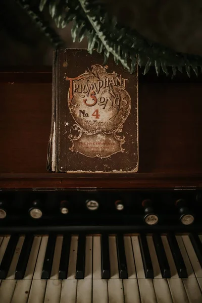 Tiro de close-up vertical de um piano vintage e um livro de partituras que diz Triumphant Songs — Fotografia de Stock