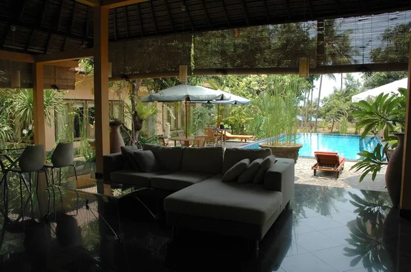 Sofá chaise ao ar livre perto de espreguiçadeiras de verão e guarda-chuvas por uma piscina cercada por plantas e árvores — Fotografia de Stock