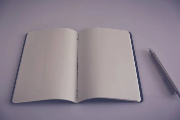 Hög vinkel skott av skrivbordet hos en poet med en öppen anteckningsbok och en silverpenna på en vit yta — Stockfoto
