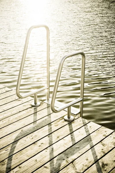 Vertikale Nahaufnahme einer silbernen Poolleiter aus Stahl auf einem hölzernen Steg am Wasser — Stockfoto