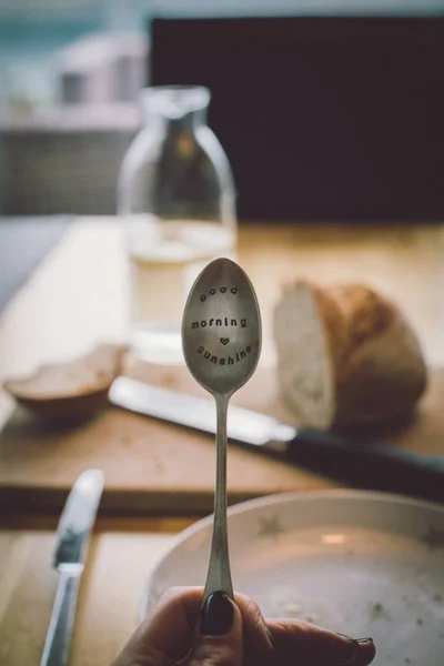 Vertical shot of a person holding a spoon with text written on it with a blurred background