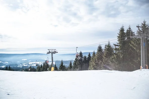 Schöne Aufnahme von Seilbahnen über dem verschneiten Hügel in der Nähe von Bäumen unter bewölktem Himmel — Stockfoto