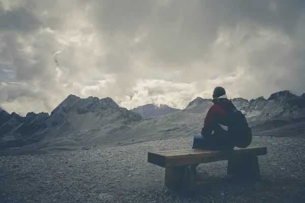 A male sitting on a wooden bench enjoying the beautiful view of mountains and the crazy sky after an exhausting day