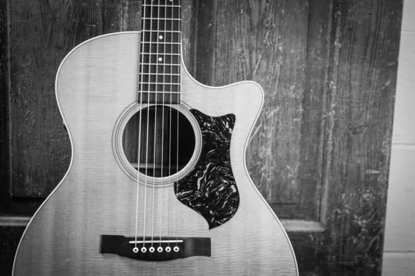 Прекрасний сірий знімок акустичної гітари, нахиленої на дерев'яні двері на дерев'яній поверхні — стокове фото
